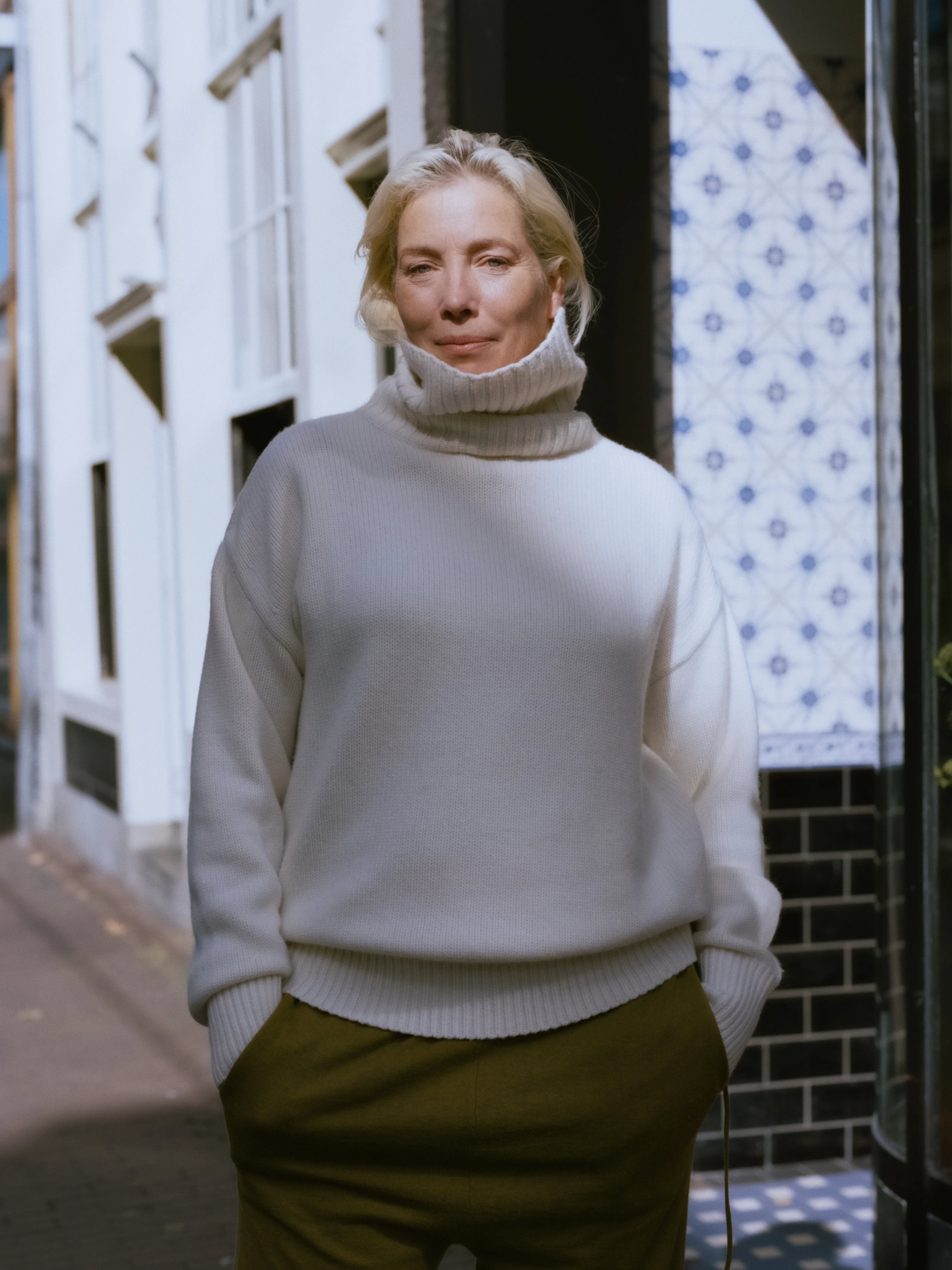woman wearing a cream heavy-knit cashmere turtleneck sweater with ribbed trims, standing outdoors.